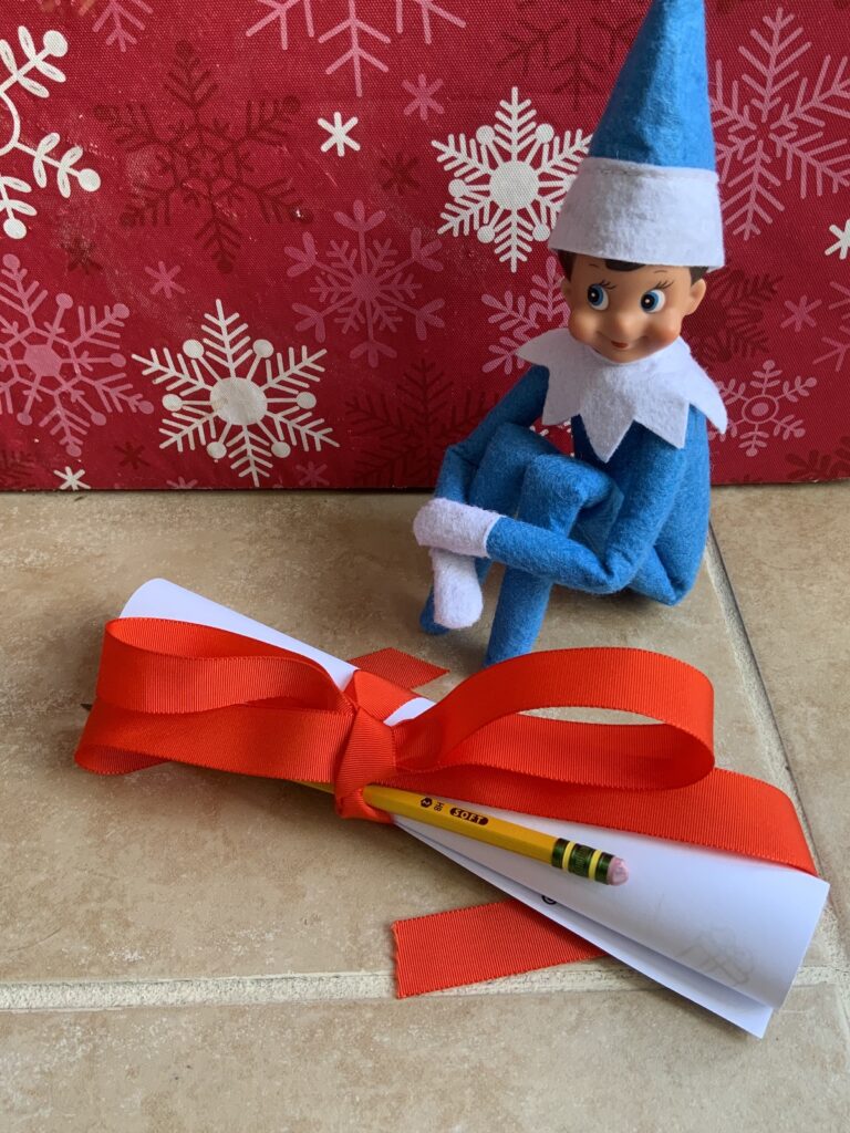 Blue elf on the shelf doll sitting with a paper tied up in a red ribbon.