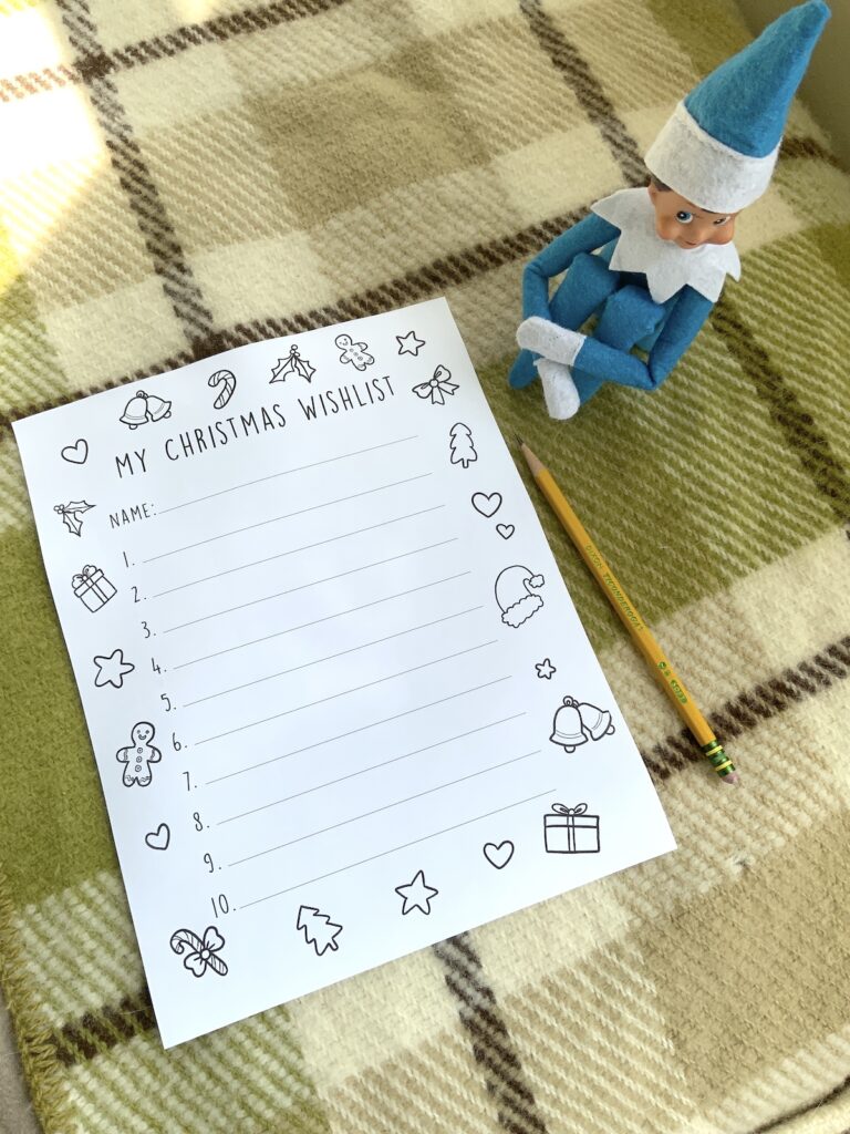 Elf sitting next to a printed out Christmas wishlist with a pencil, on a woolen blanket.