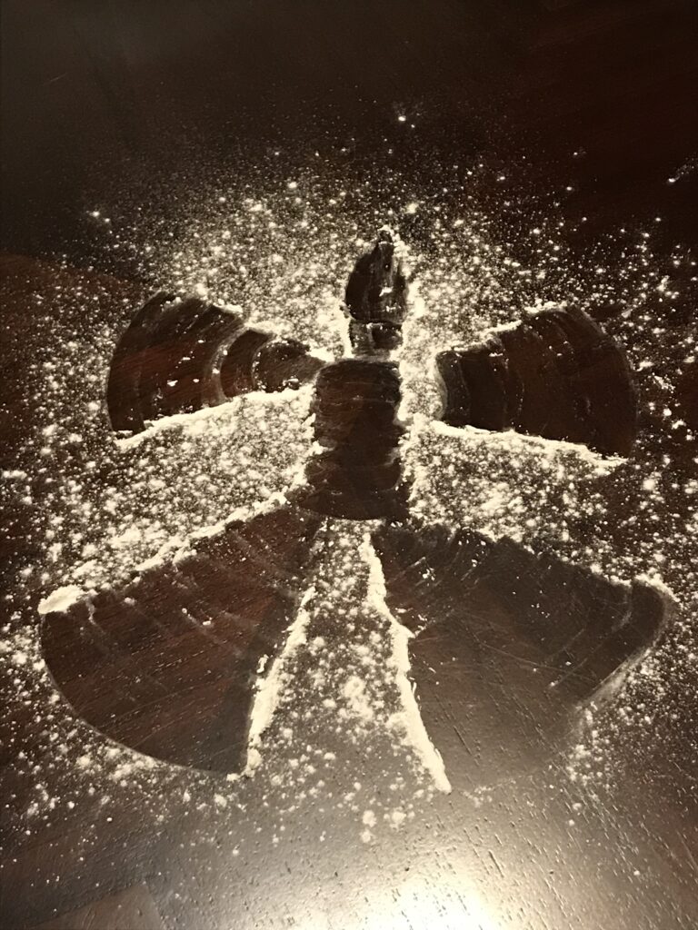 An elf-doll sized snow angel image made into sprinkled flour on a table.
