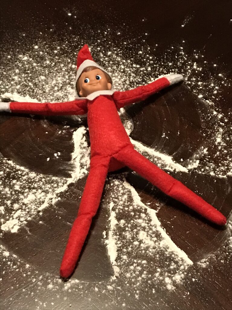 Elf doll placed on top of the fake snow angel on a table.