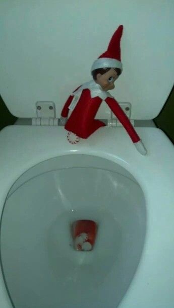 An elf on the shelf doll sitting on the back of a toilet with peppermint candies falling into the toilet.