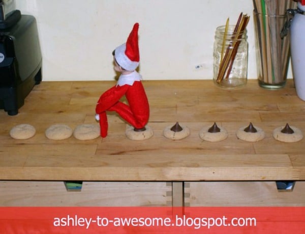 an elf on the shelf doll sitting on Christmas cookies to make it look like he's pooping chocolate on them.