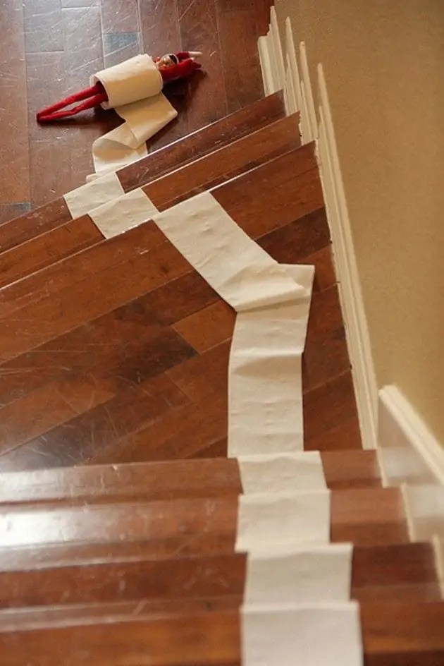 An elf on the shelf doll rolling down the stairs in toilet paper.