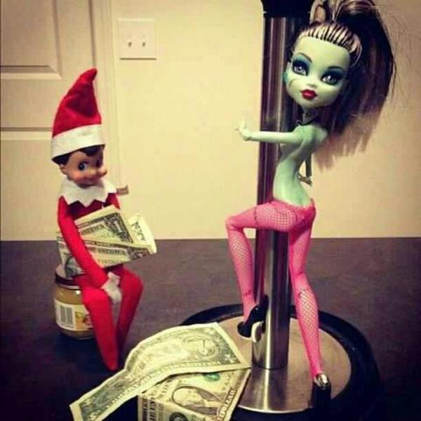 An elf on the shelf doll holding dollar bills while a monster high doll does a dance on a paper towel holder.