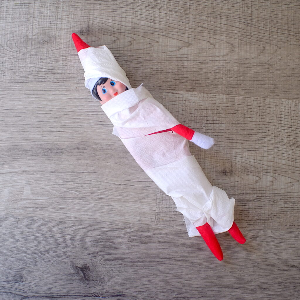 An elf on the shelf doll wrapped up in toilet paper to look like a mummy.