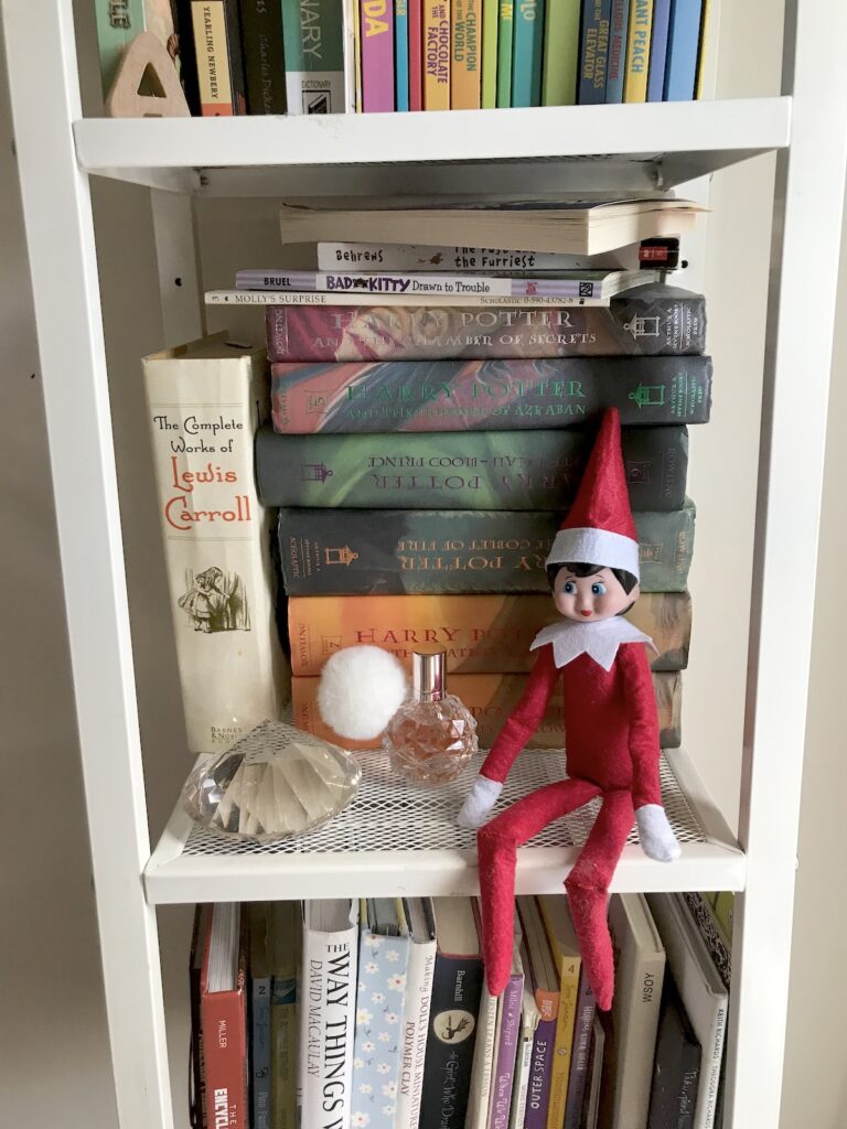 An elf on the shelf doll sitting in a shelf.