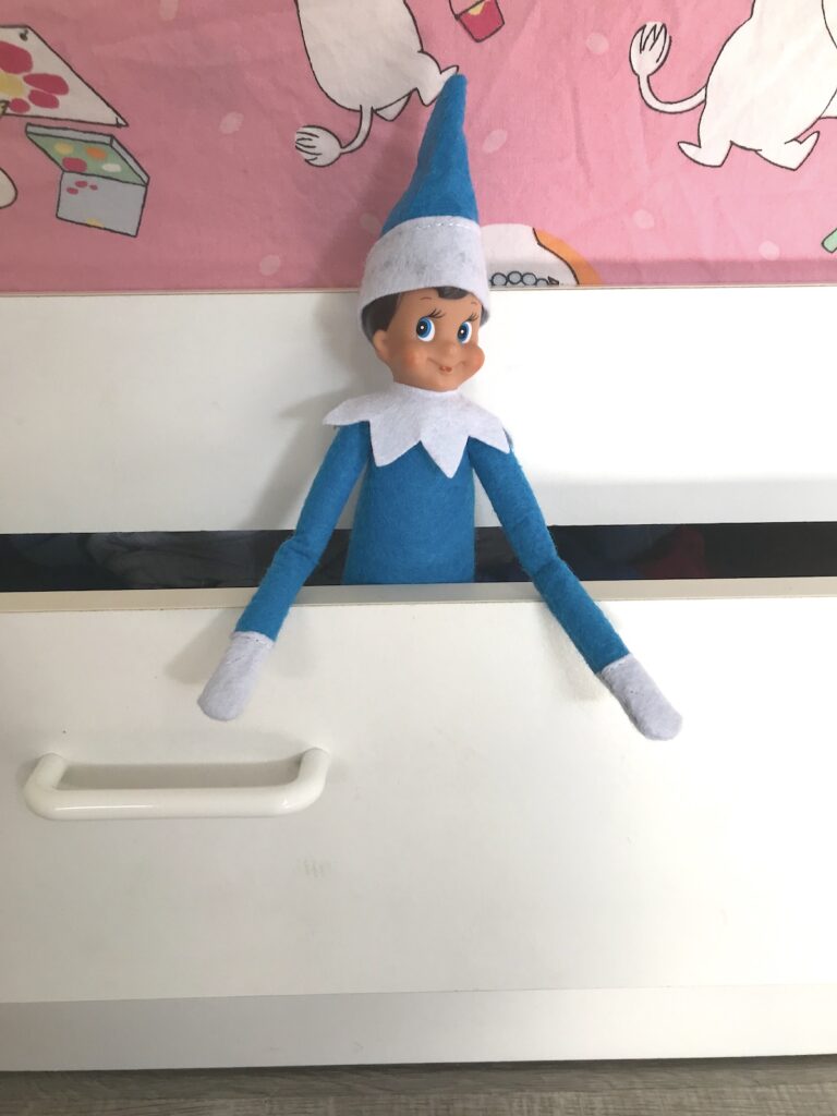 An elf on the shelf doll popping out from a dresser drawer.