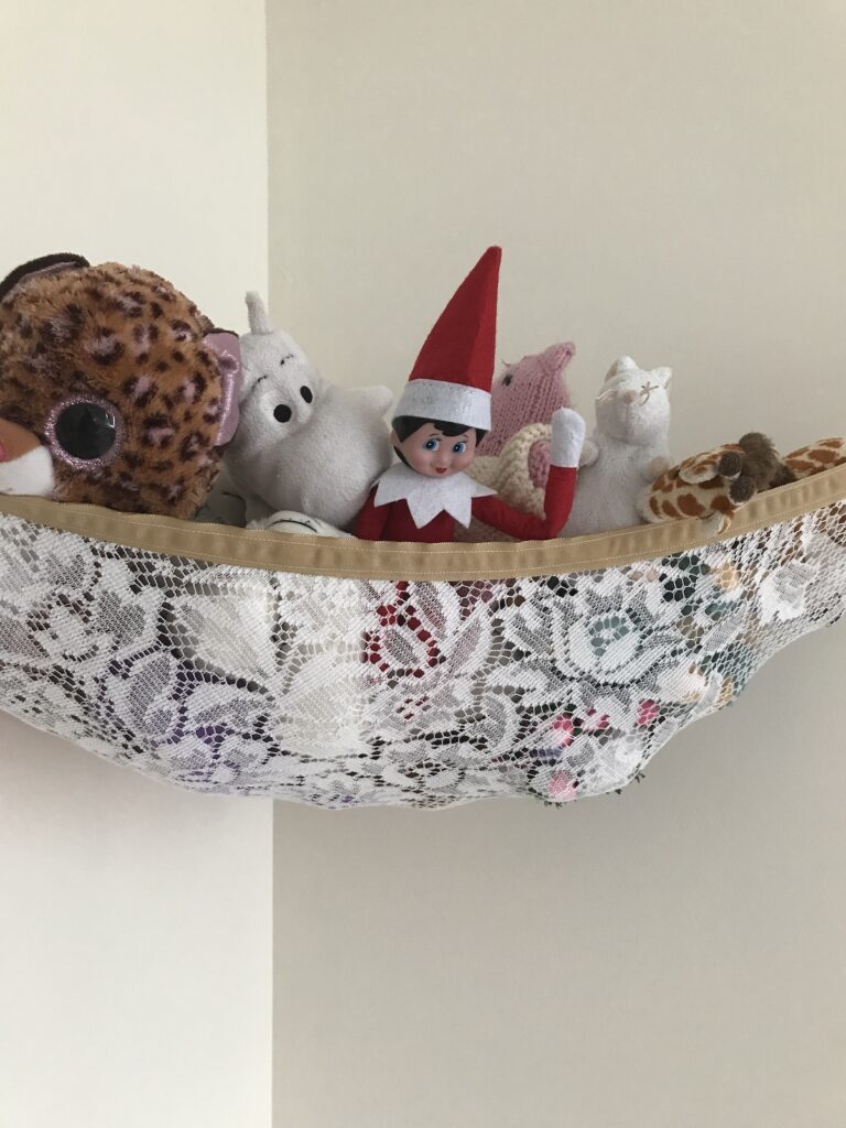 an elf on the shelf doll in a hammock of stuffed animals